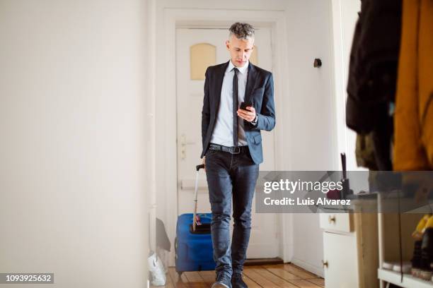 mature businessman walking with his luggage using mobile phone - denim arrivals stock pictures, royalty-free photos & images