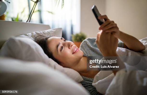 woman in her bed checking phone - aufwachen stock-fotos und bilder