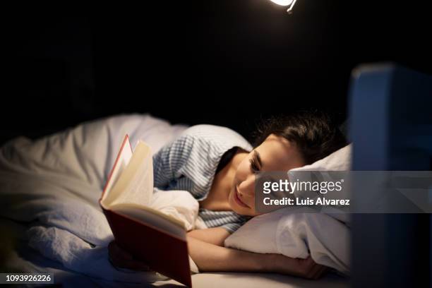 woman reading book in bed - reading stock-fotos und bilder