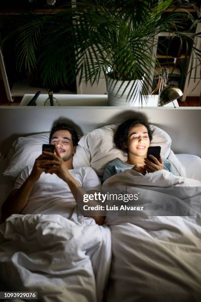 happy young couple using phones in bed - instagram husband stock pictures, royalty-free photos & images