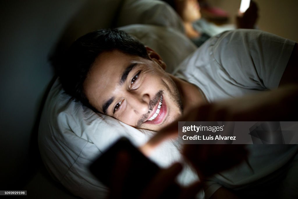 Man in bed checking his social media status on smartphone