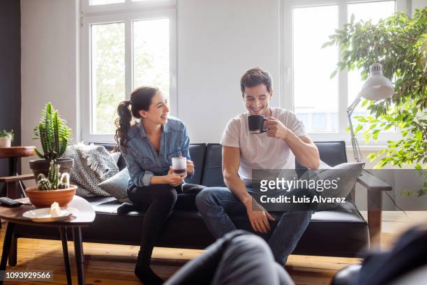 couple having coffee together in living room - couple photos et images de collection