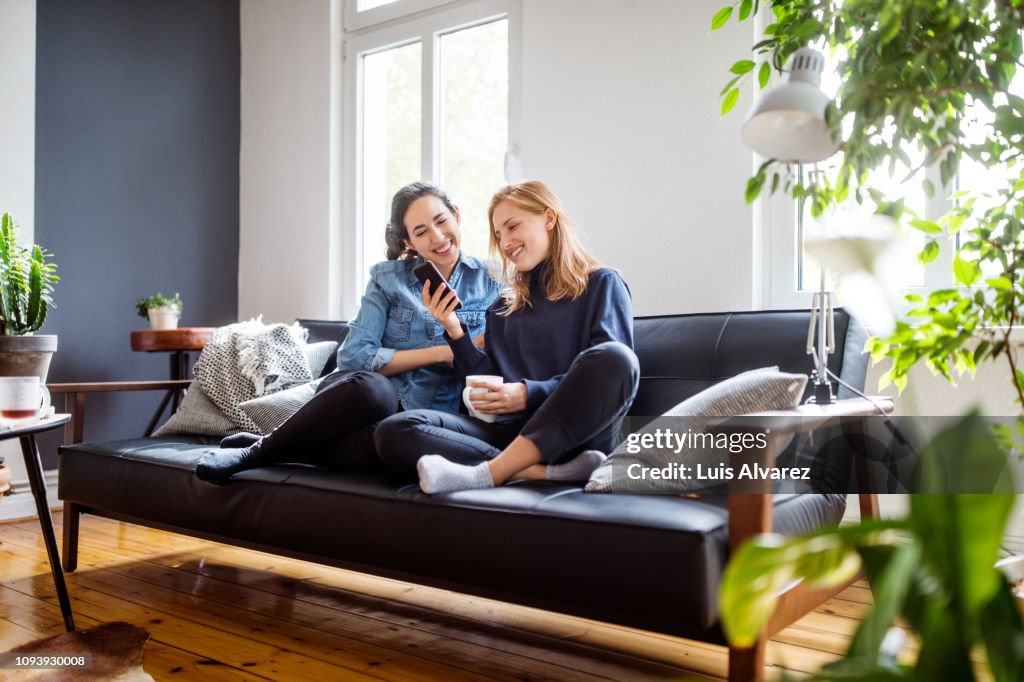 Women friends relaxing at home using smart phone
