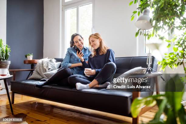 women friends relaxing at home using smart phone - sofa stock-fotos und bilder