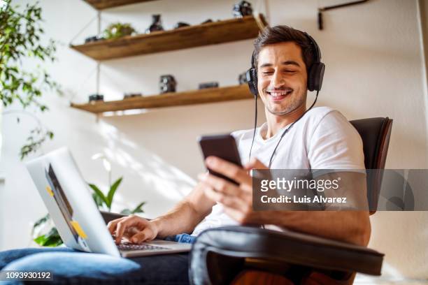 man listening music while working on laptop - listening stock-fotos und bilder