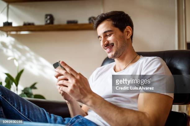 young man using smart phone at home - jeunes hommes photos et images de collection
