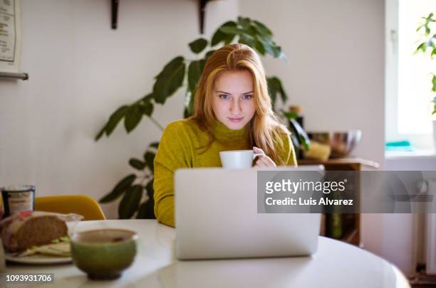 woman drinking coffee and using laptop at home - young blonde woman facing away photos et images de collection