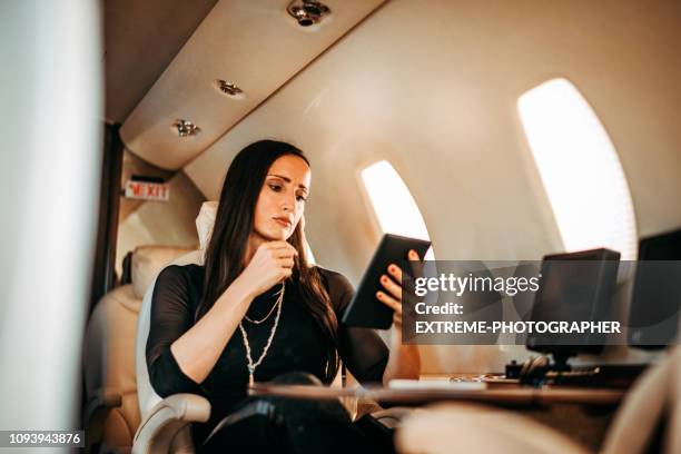 rich and successful female using a digital tablet while sitting in a private airplane - billionaire stock pictures, royalty-free photos & images
