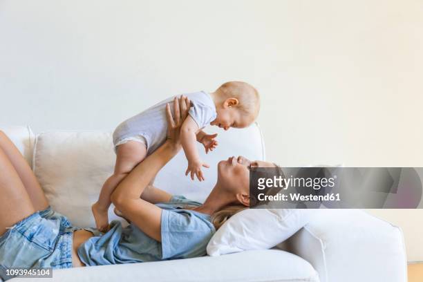 mother lying on couch holding her baby girl - baby stock-fotos und bilder