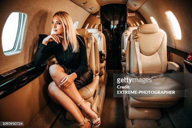 rich blond woman looking through window and thinking while traveling aboard a private airplane - billionaire stock pictures, royalty-free photos & images