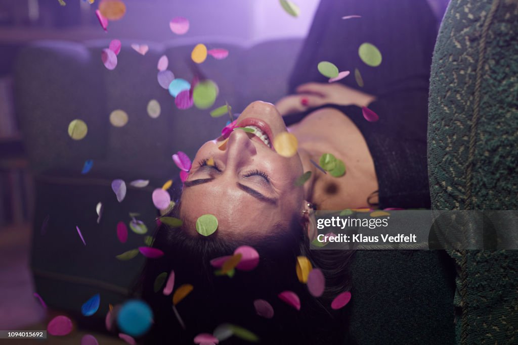 Young woman laying on sofa with confetti falling