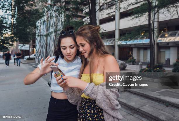 friends using smart phone while standing on sidewalk in city - bauchfreies oberteil stock-fotos und bilder