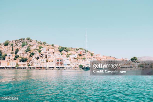 houses on mountain by sea against clear blue sky during sunny day - symi ストックフォトと画像