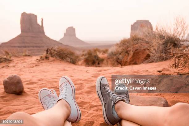 low section of friends sitting on sand at monument valley tribal park against sky - pov shoes stock pictures, royalty-free photos & images