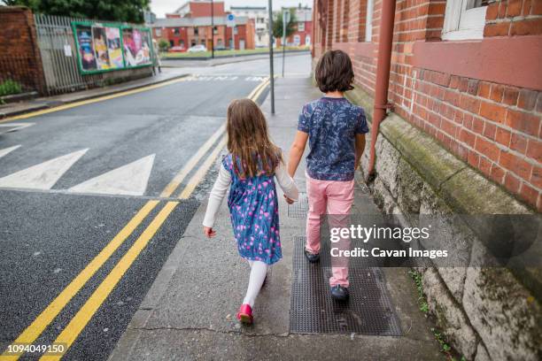 rear view of siblings holding hands while walking at sidewalk in city - irish family stock pictures, royalty-free photos & images