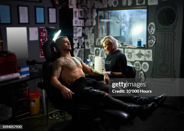 young man reclining in chair having new tattoo - tattooing stock-fotos und bilder