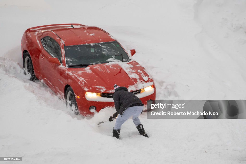 A man digs out a red Chevrolet car from the parking lot snow...