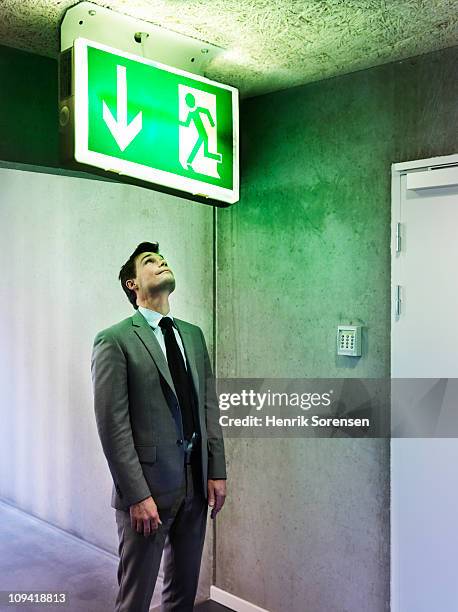 businessman looking at oversized exit sign - uitgang stockfoto's en -beelden