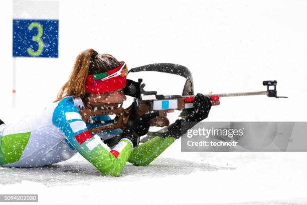 rear view of female biathlon competitor practicing target shooting in snowstorm - biathlon ski stock pictures, royalty-free photos & images