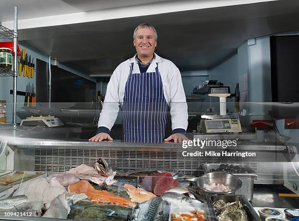 male fishmonger standing by counter - fishmonger stock pictures, royalty-free photos & images