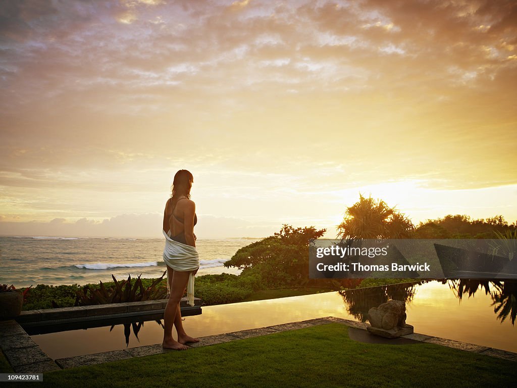 Woman standing near edge of pool at sunrise