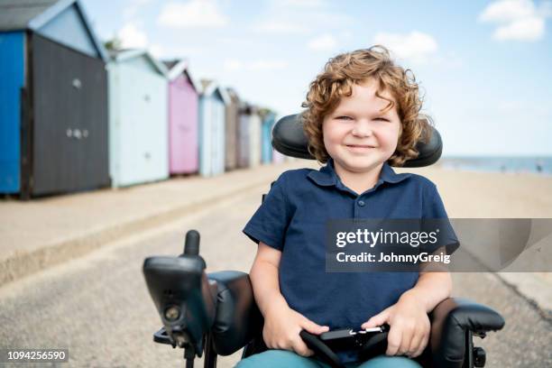 behinderte junge sitzen im rollstuhl durch strandhütten - child in wheelchair stock-fotos und bilder