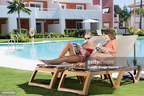 two women sunbathing on sunloungers reading magazines - magazine retreat day 2 stock pictures, royalty-free photos & images