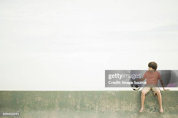 boy sitting on wall with football - boy sitting stock pictures, royalty-free photos & images