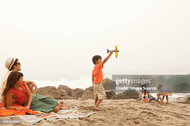 family on beach, boy playing with toy plane - beach picnic stock pictures, royalty-free photos & images