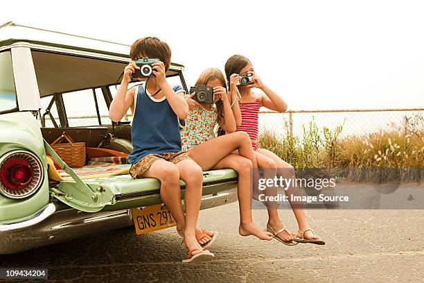 three children sitting on back of estate car taking photographs - vintage car stockfoto's en -beelden