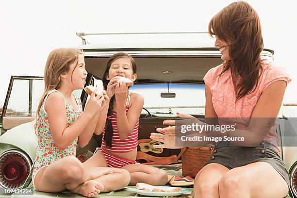 mother and daughters eating sandwiches on car boot - eating in car stock pictures, royalty-free photos & images