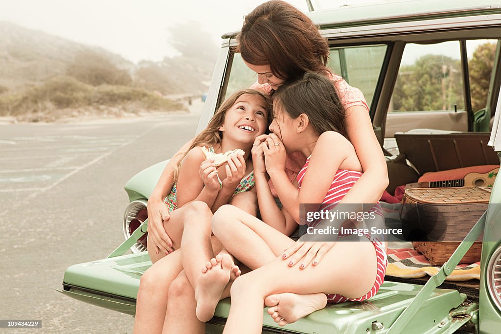 Mother and daughters eating sandwiches on car boot