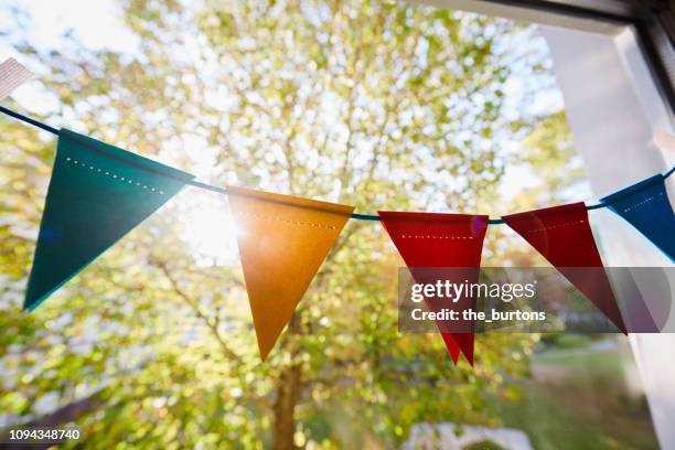 colorful bunting flags hanging at the window/ pennant chain for party decoration - pennant stock-fotos und bilder