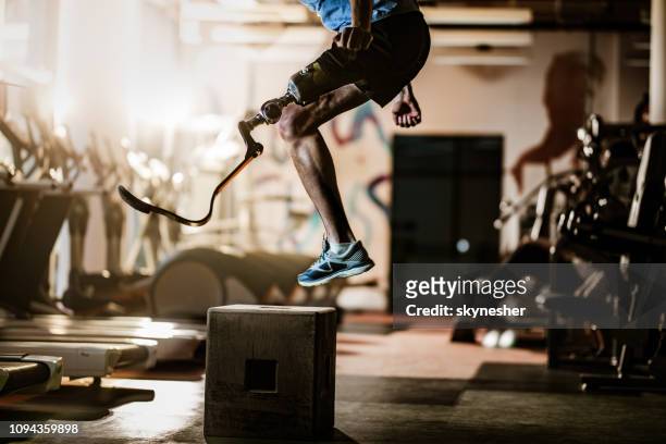 Unrecognizable amputee jumping on crate during cross training in a gym.