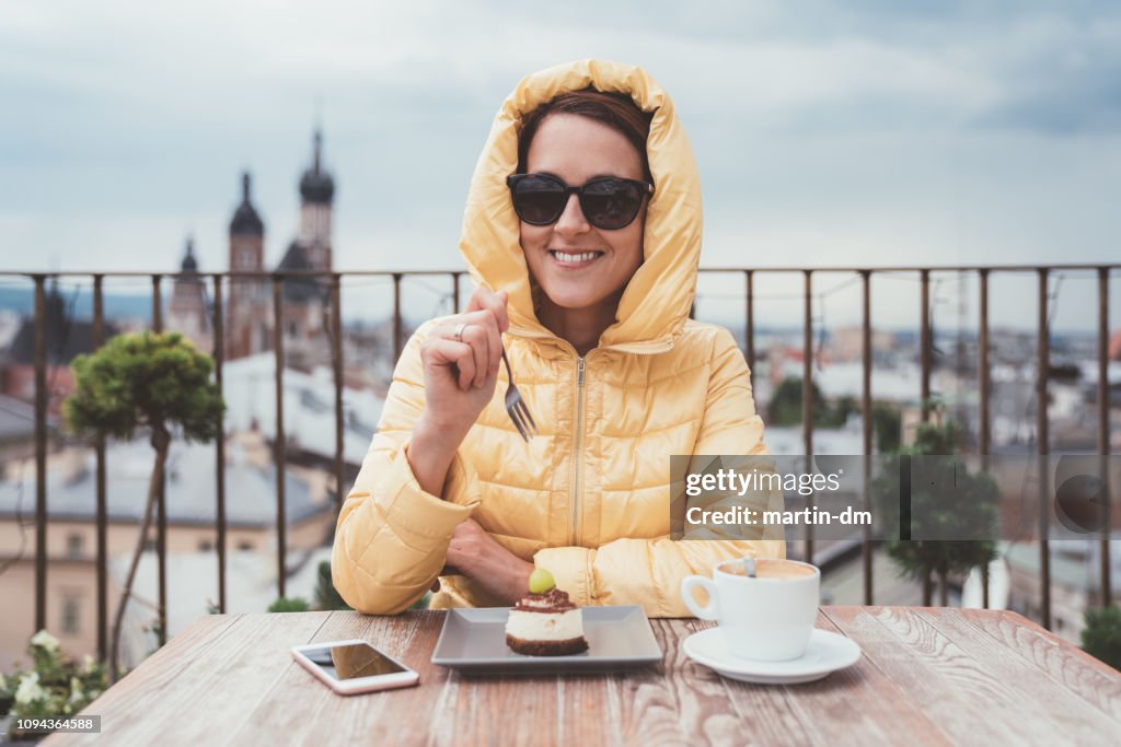 Happy woman eating dessert with coffee on rooftop