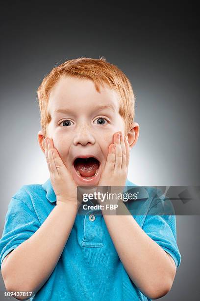 portrait of smiling redhead boy (4-5) wearing blue polo shirt and looking surprised, studio shot - red hair boy and freckles stock-fotos und bilder