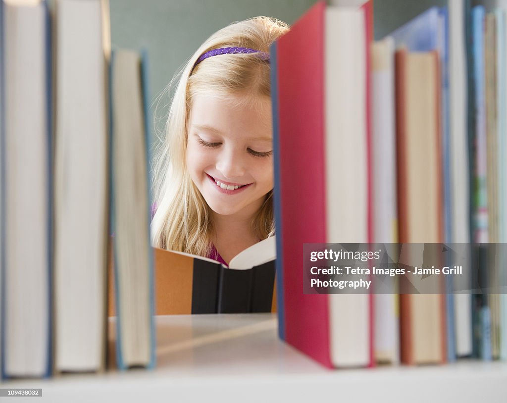 USA, New Jersey, Jersey City, View across the shelf showing girl (8-9) reading book