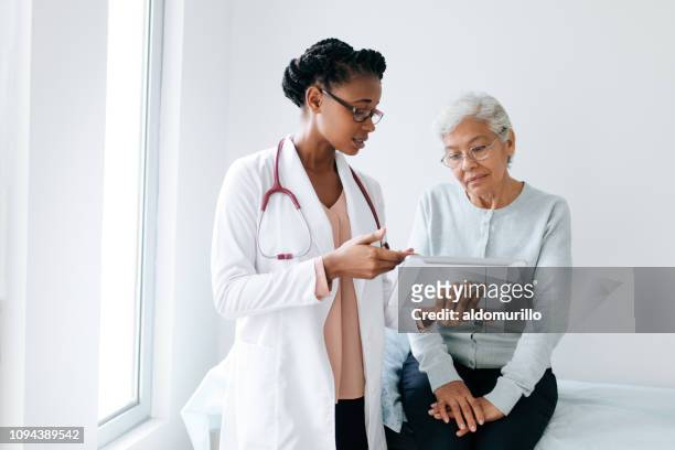 doctora negra mostrando tableta digital al paciente mayor - explicar fotografías e imágenes de stock
