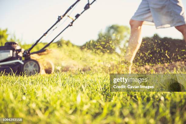 low section of man mowing grassy field in yard against sky during sunset - segadora fotografías e imágenes de stock