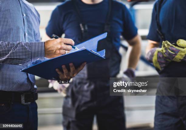 foreman irreconocible pasando por papeles con los obreros en un almacén. - clipboard fotografías e imágenes de stock