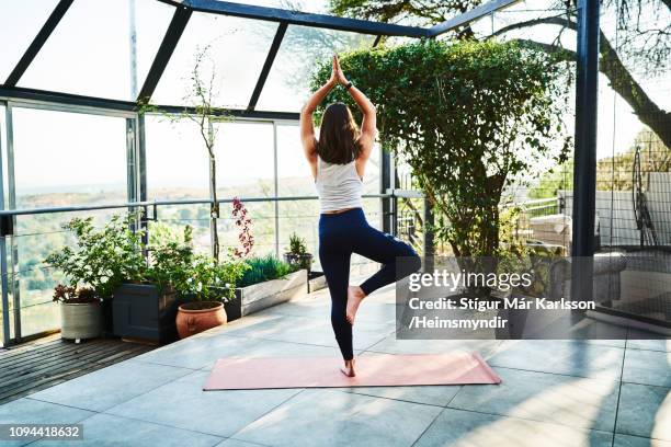 young woman practicing tree pose on exercise mat - tree position stock pictures, royalty-free photos & images