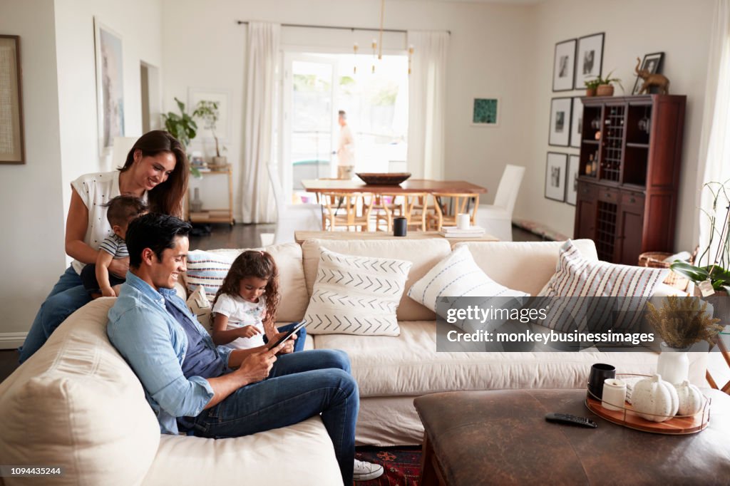 Young Hispanic family sitting on sofa reading a book together in their living room