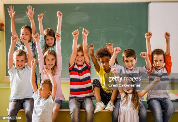 joyful elementary students with raised arms in the classroom. - finale celebration stock pictures, royalty-free photos & images