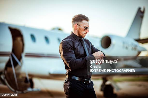 rich and successful young businessman looking at his watch in front of a private airplane - billionaire stock pictures, royalty-free photos & images