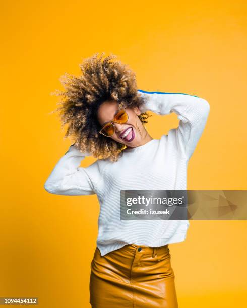 aufgeregt afro junge frau tanzt vor gelbem hintergrund - frau sommerlich studioaufnahme stock-fotos und bilder