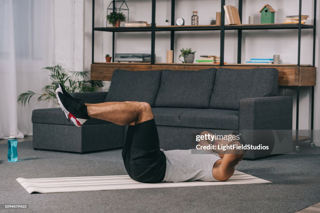 Hombre de raza mixta haciendo ejercicios en estera de fitness en sala de estar