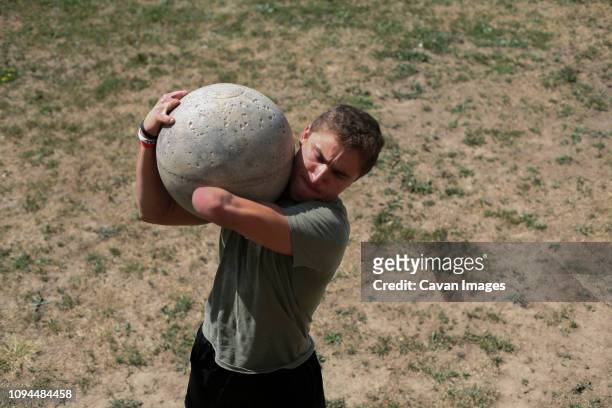 High angle view of disabled male athlete carrying atlas stone while standing on field during sunny day