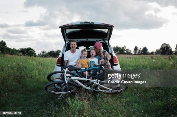 happy family with bicycles sitting on car trunk amidst grassy field against cloudy sky - boots stock pictures, royalty-free photos & images