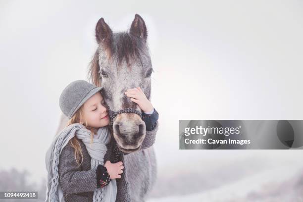 cute girl embracing pony against sky during winter - pony paard stockfoto's en -beelden