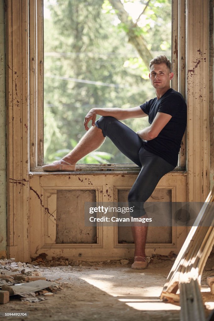 Side view of male ballet dancer sitting on window sill in old building